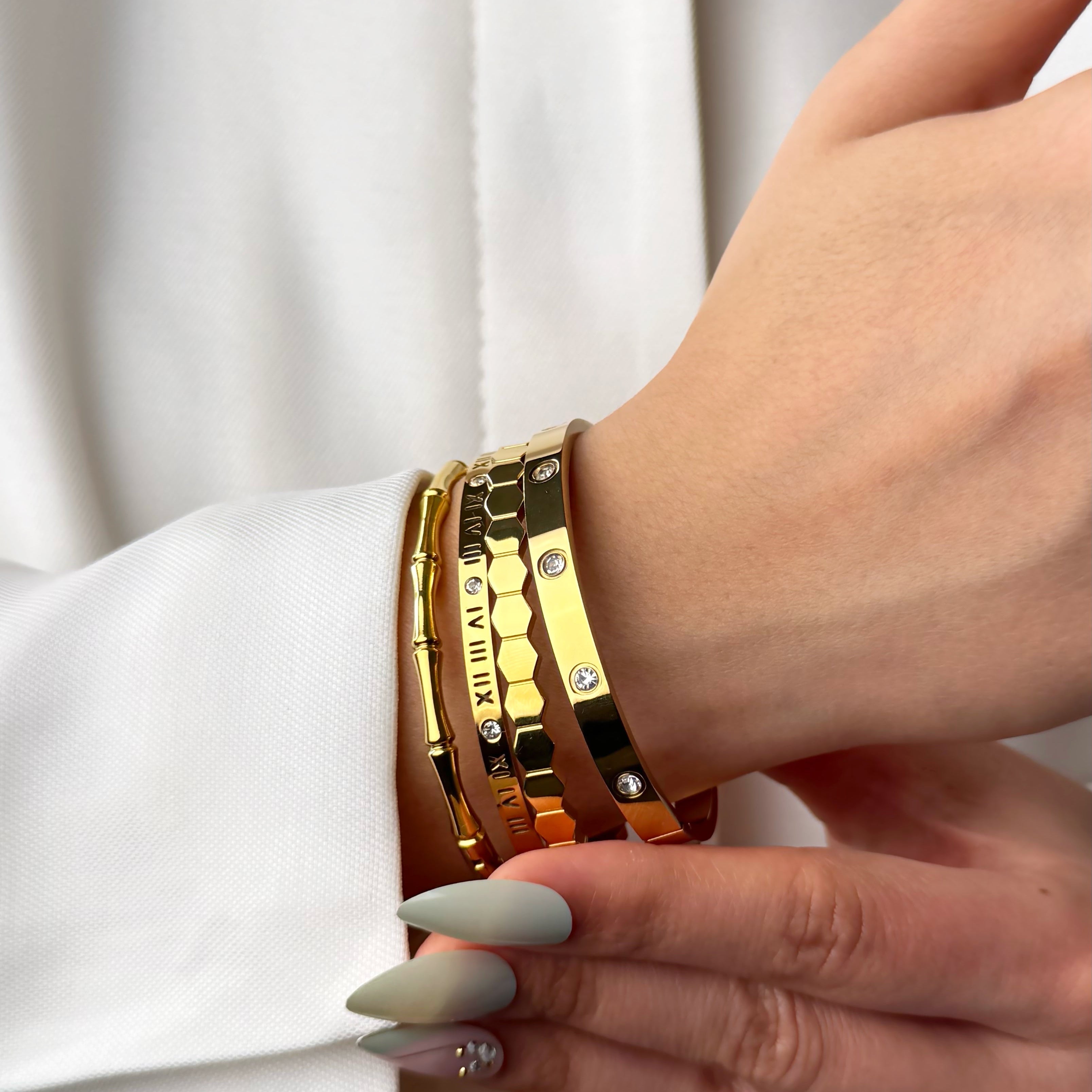 Gold diamond, hexagon, roman and bamboo bangle bracelets on a wrist by Noble Aura UK