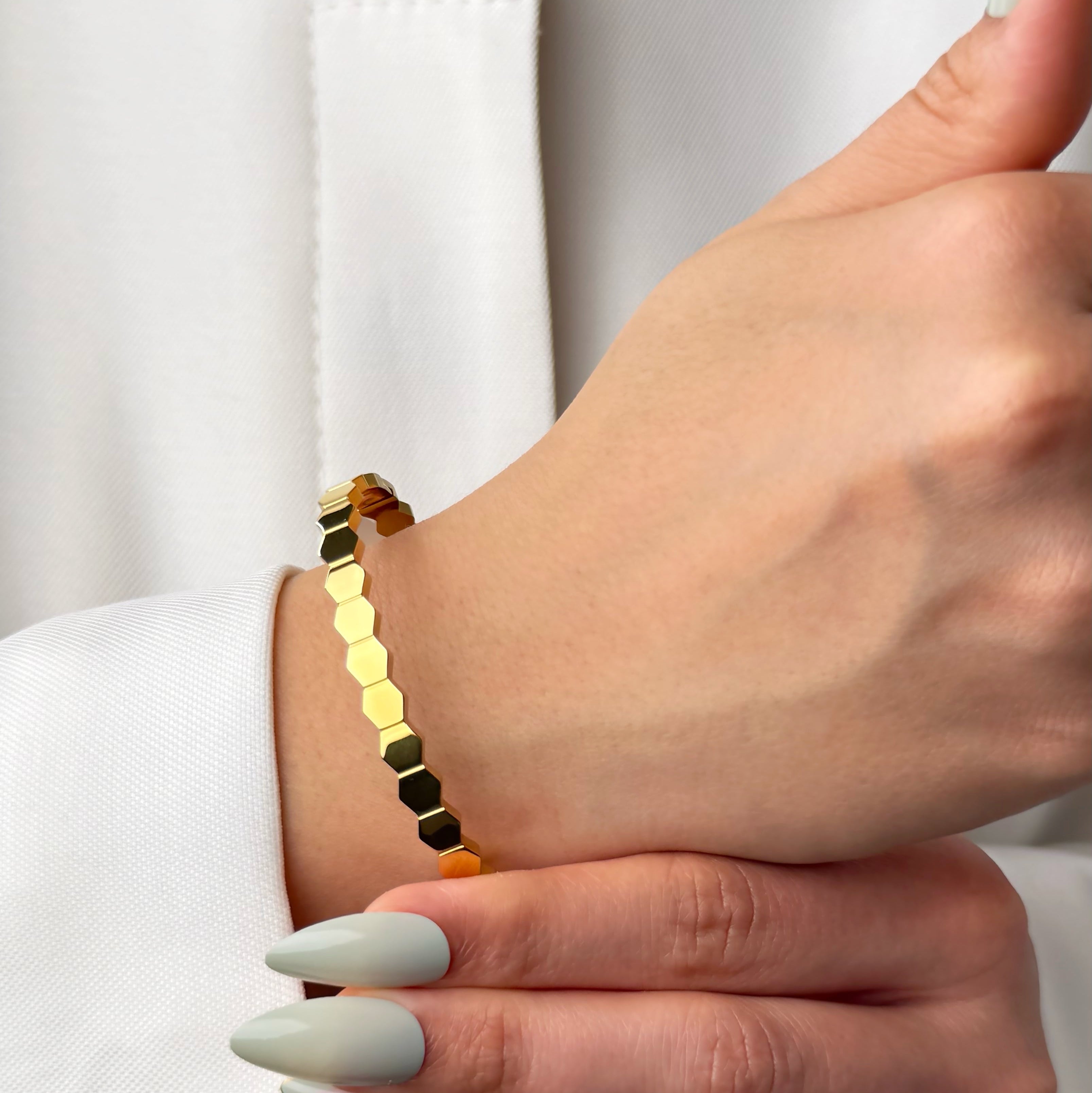 Hand wearing a gold hexagonal bead bracelet with a neutral background